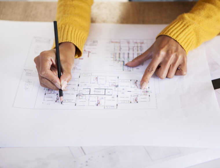 Close-up of young adult latin architect leaning on desk while working on blueprint in studio